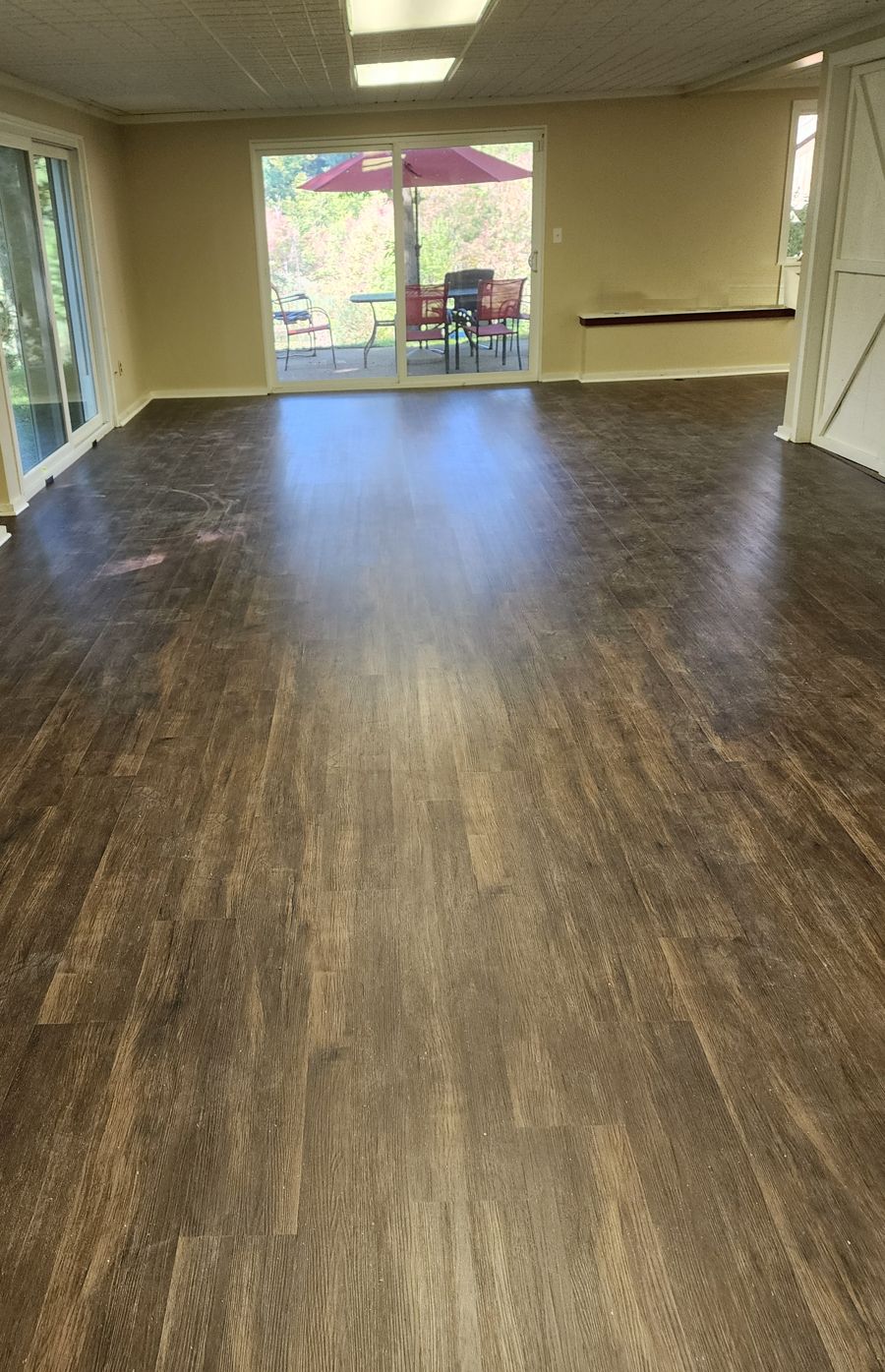 Finished basement with rich brown wood-look luxury vinyl plank flooring leading to sliding glass doors