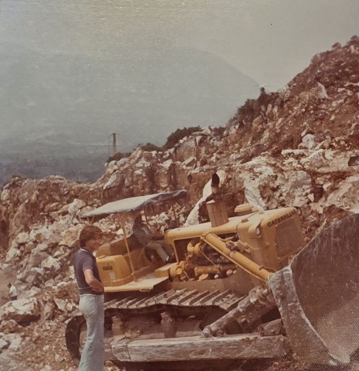 My cousin beside a bulldozer at the quarry, mountains in the haze behind