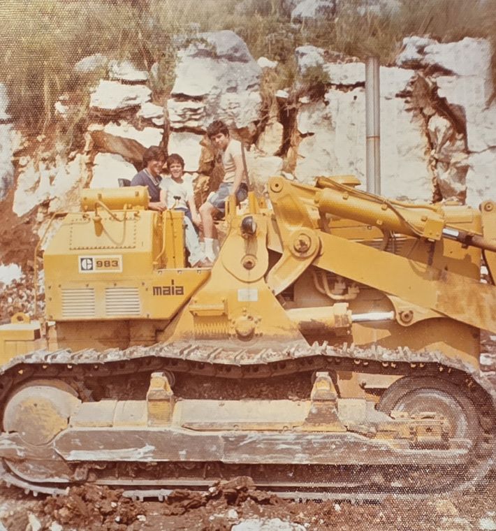 My cousin, my brother and me sitting up on the loader against the white stone wall